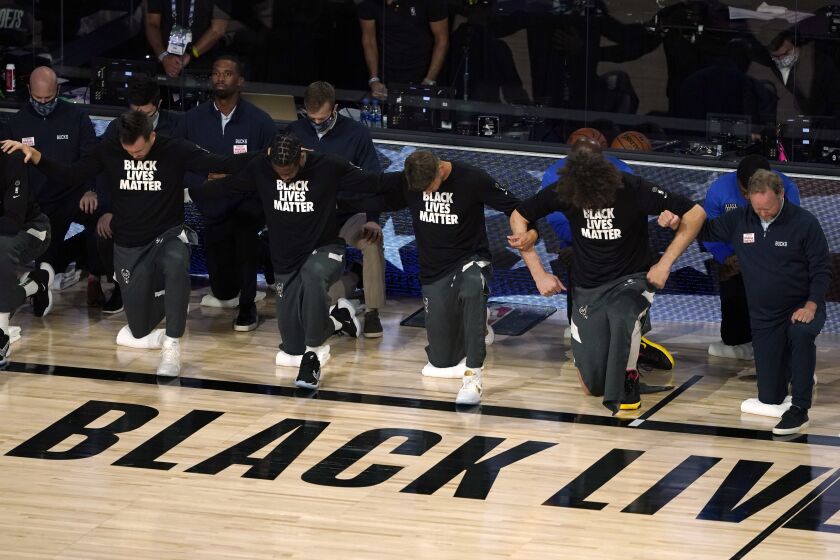 Members of the Milwaukee Bucks join arms as they kneel during the national anthem before an NBA basketball first round playoff game against the Orlando Magic Saturday, Aug. 29, 2020, in Lake Buena Vista, Fla. (AP Photo/Ashley Landis)