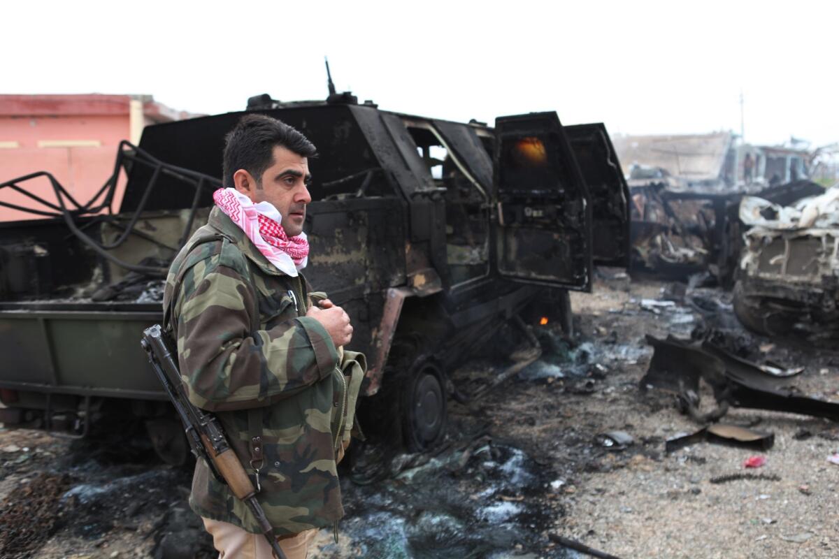 A member of the Kurdish forces stands next to an armored vehicle destroyed during the push toward Mt. Sinjar.