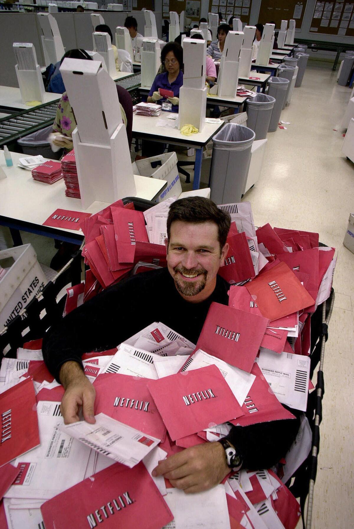 Netflix chief executive Reed Hastings sits in a mail delivery case of thousands of DVDs at their distribution plant in San Jose, Calif.