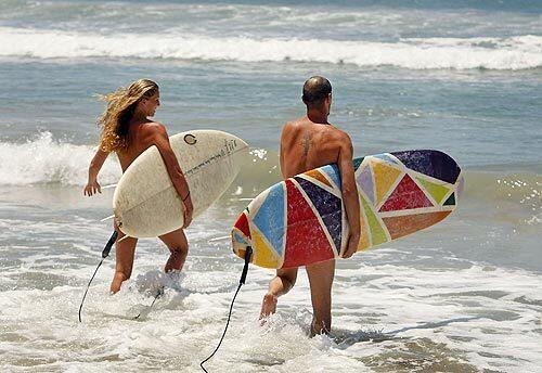 Lindsey Gage and her husband, Daniel, of Costa Mesa run into the surf to catch some waves in the buff near Trail 6 at San Onofre State Beach, where they joined a crowded beach of naturists.
