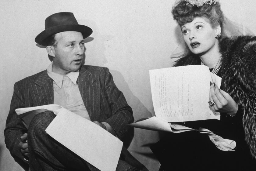 circa 1945: EXCLUSIVE American actors Bing Crosby and Lucille Ball sit with scripts in their laps. Crosby wears a pinstriped jacket with glen plaid trousers and a hat; Ball wears a dark dress with a fur coat and pearls. (Photo by Metronome/Getty Images)