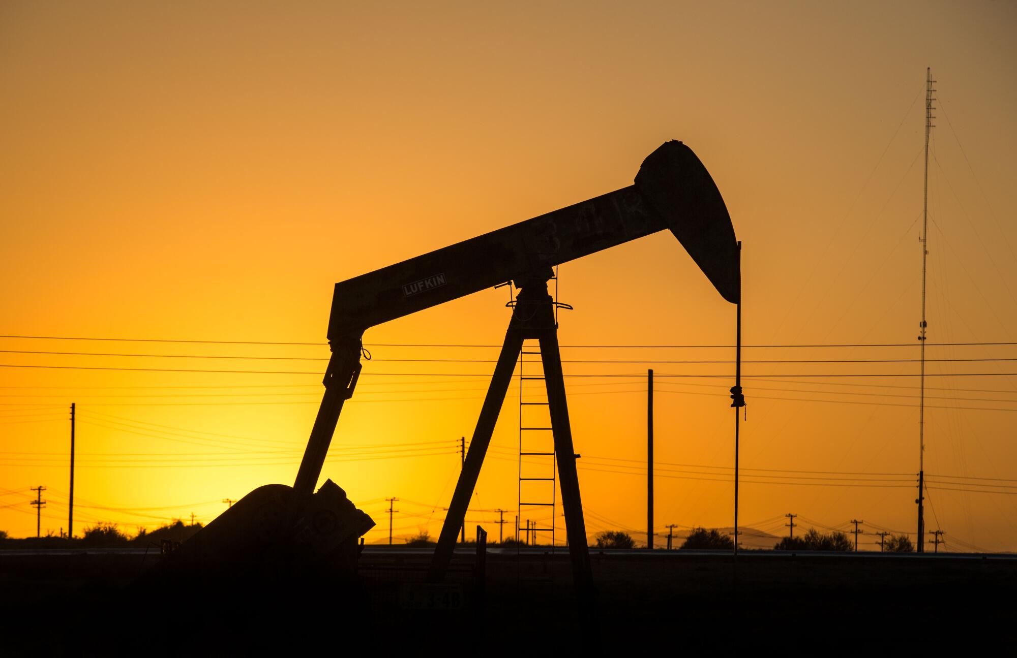 An oil pumpjack is silhouetted against a sunrise.