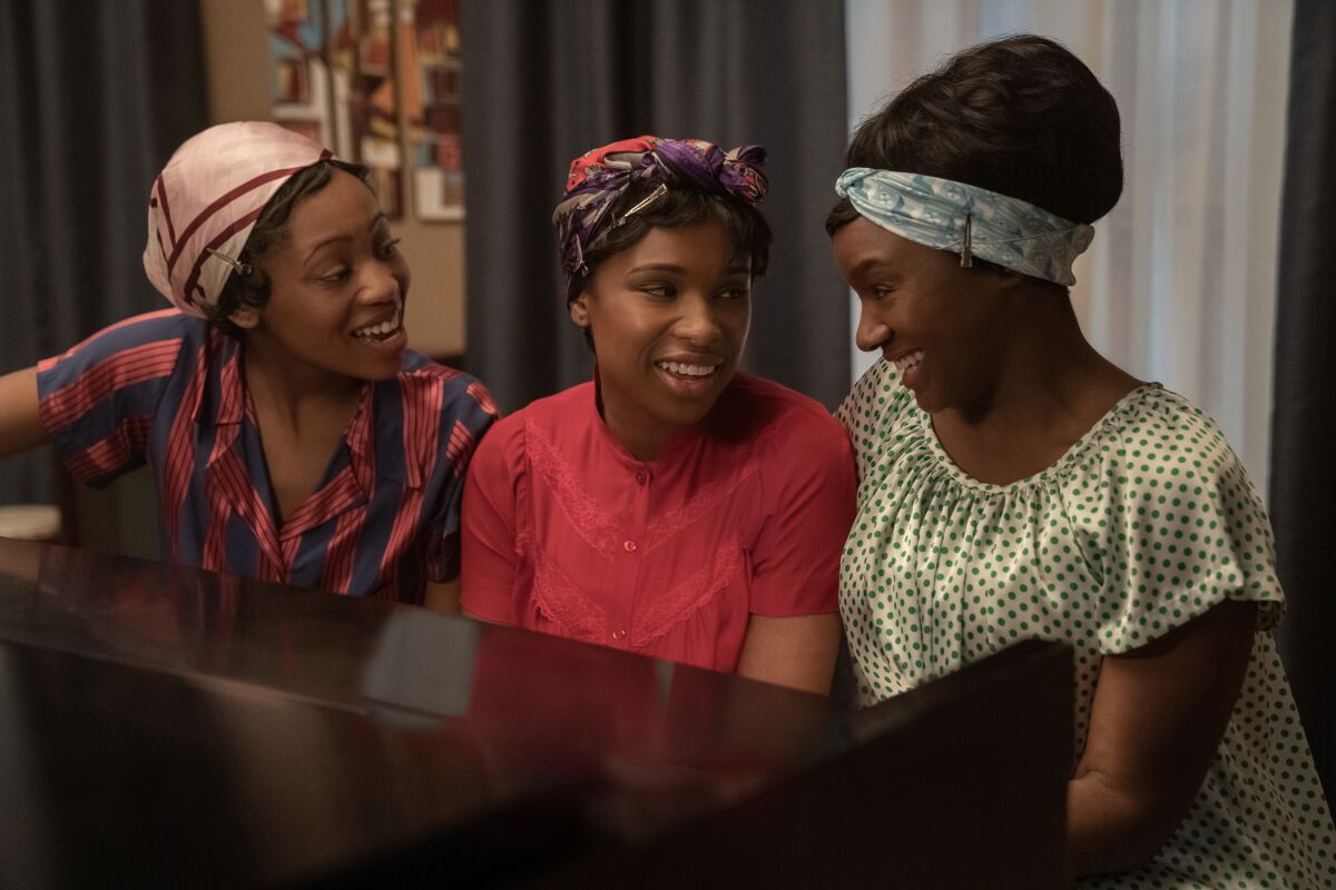 Three Black women sit together at a piano.