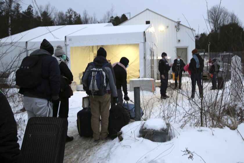 Migrantes hacen una fila en la frontera entre Estados Unidos y Canadá, en un centro de recepción para personas que cruzan a territorio canadiense sin autoridad legal, en Saint-Bernard-de-Lacolle, Quebec, Canadá, el miércoles 12 de enero de 2022, en una fotografía tomada desde Champlain, Nueva York. (AP Foto/Wilson Ring)