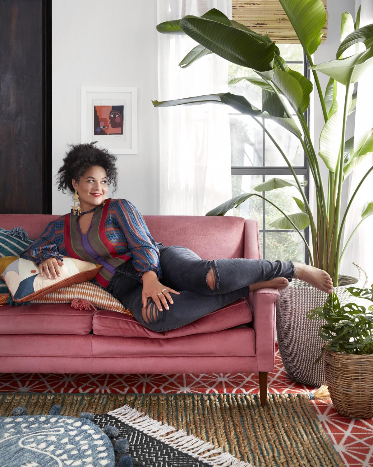 Designer Justina Blakeney reclines on a couch at home with her plants.