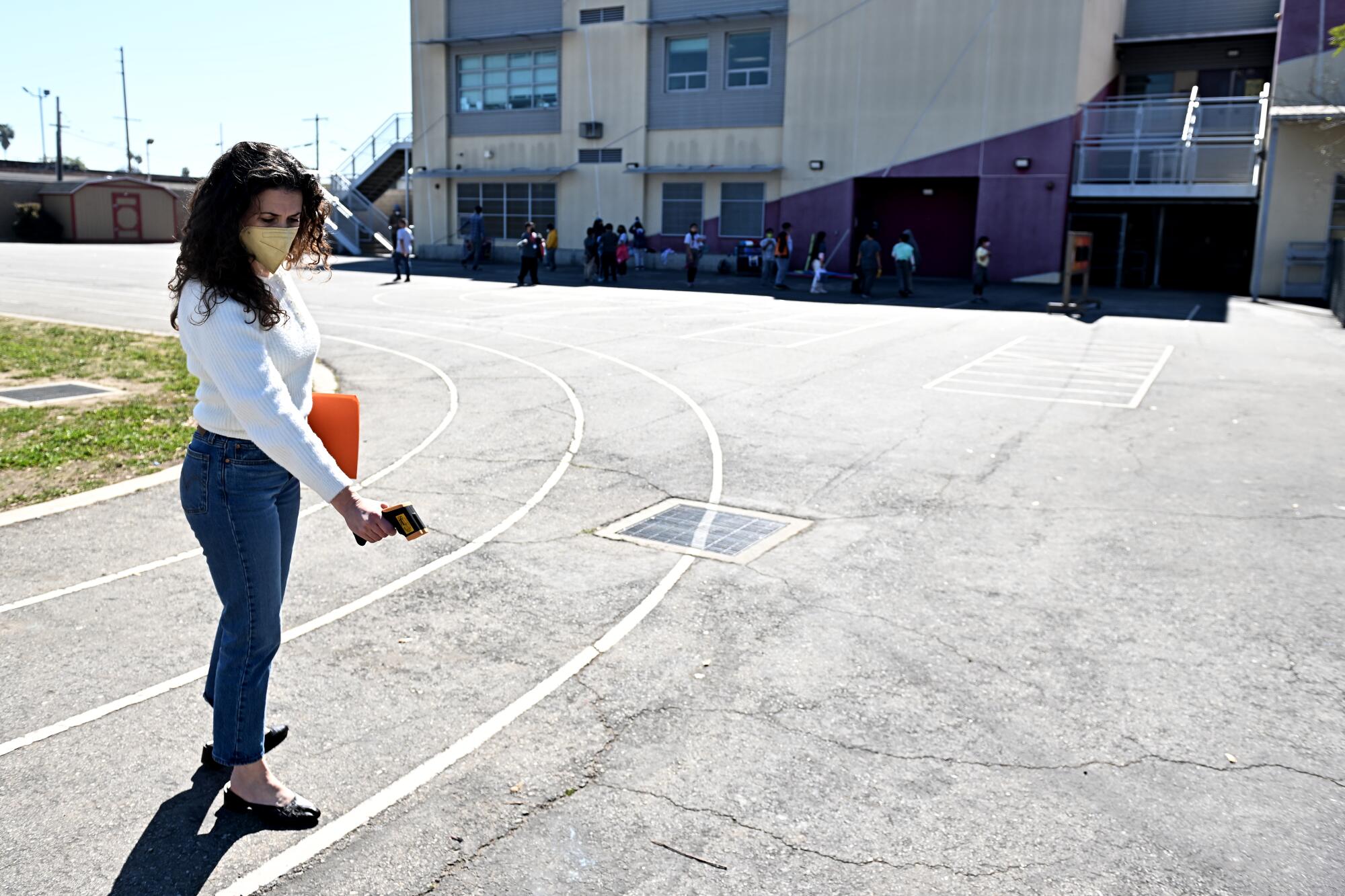 A woman uses an electronic device to measure the temperature of asphalt at a school. 