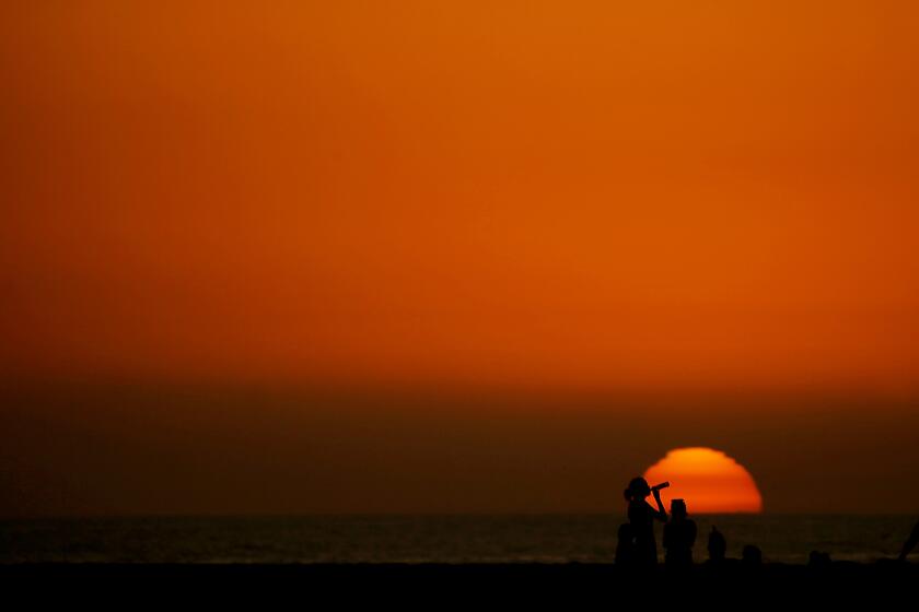 HUNTINGTON BEACH, CALIF. - DEC. 6, 2023. Beachgoers are framed against the setting sun at the end of a warm day in Huntington Beach. Scientists say that Novemeber was the sixth straight month to set a heat record. (Luis Sinco / Los Angeles Times)