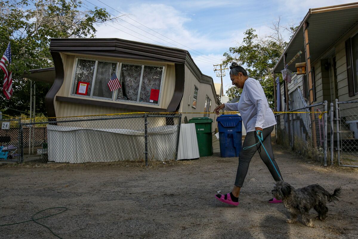 A woman walking her dog passes a mobile home buckled by an earthquake