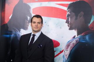 A man in a black suit posing in front of a giant poster of Batman and Superman staring at each other