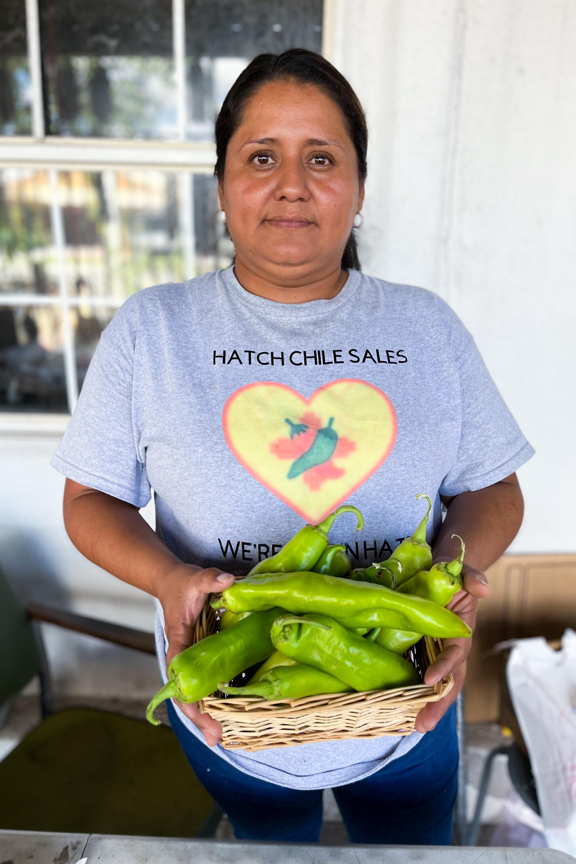 A woman with dark hair, in a gray T-shirt, holds a bowl of large green chiles