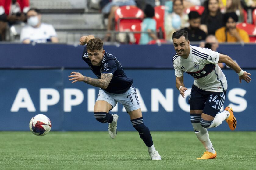 Sporting Kansas City's Marinos Tzionis (77) and Vancouver Whitecaps' Luís Martins (14) chase the ball during the first half of an MLS soccer match Saturday, June 3, 2023, in Vancouver, British Columbia. (Ethan Cairns/The Canadian Press via AP)