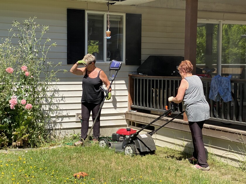 A woman sizes up a weed as another mows a lawn