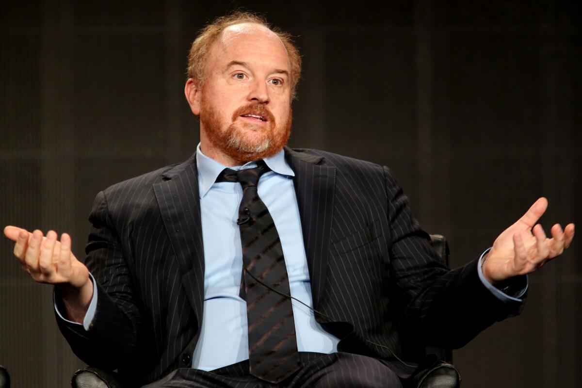 Louis C.K., in a suit and tie, sits back in his seat with his hands outstretched.