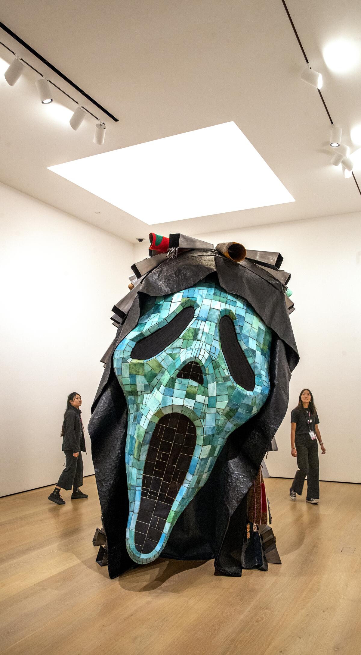 A view of a large-scale sculpture showing the mask from the "Scream" movies rendered in turquoise and cow bells
