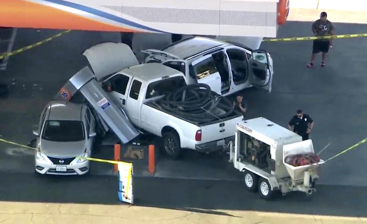 Yellow police tape surrounds a pickup truck that crashed into a couple of vehicles and a toppled fuel pump