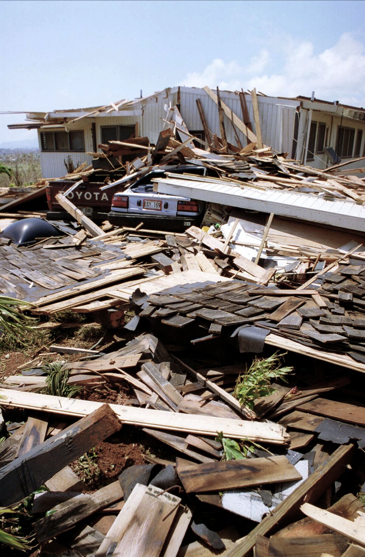A car and a pickup truck are buried under the rubble of a home severely damaged by a hurricane