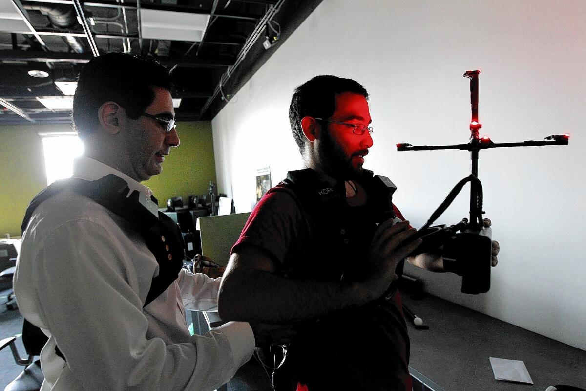 Shahriar Afshar, president and founder of Immerz, left, helps Fotos Frangoudes, technical director for Virtual Pyedog, suit up for a demonstration of virtual reality technology at USC.