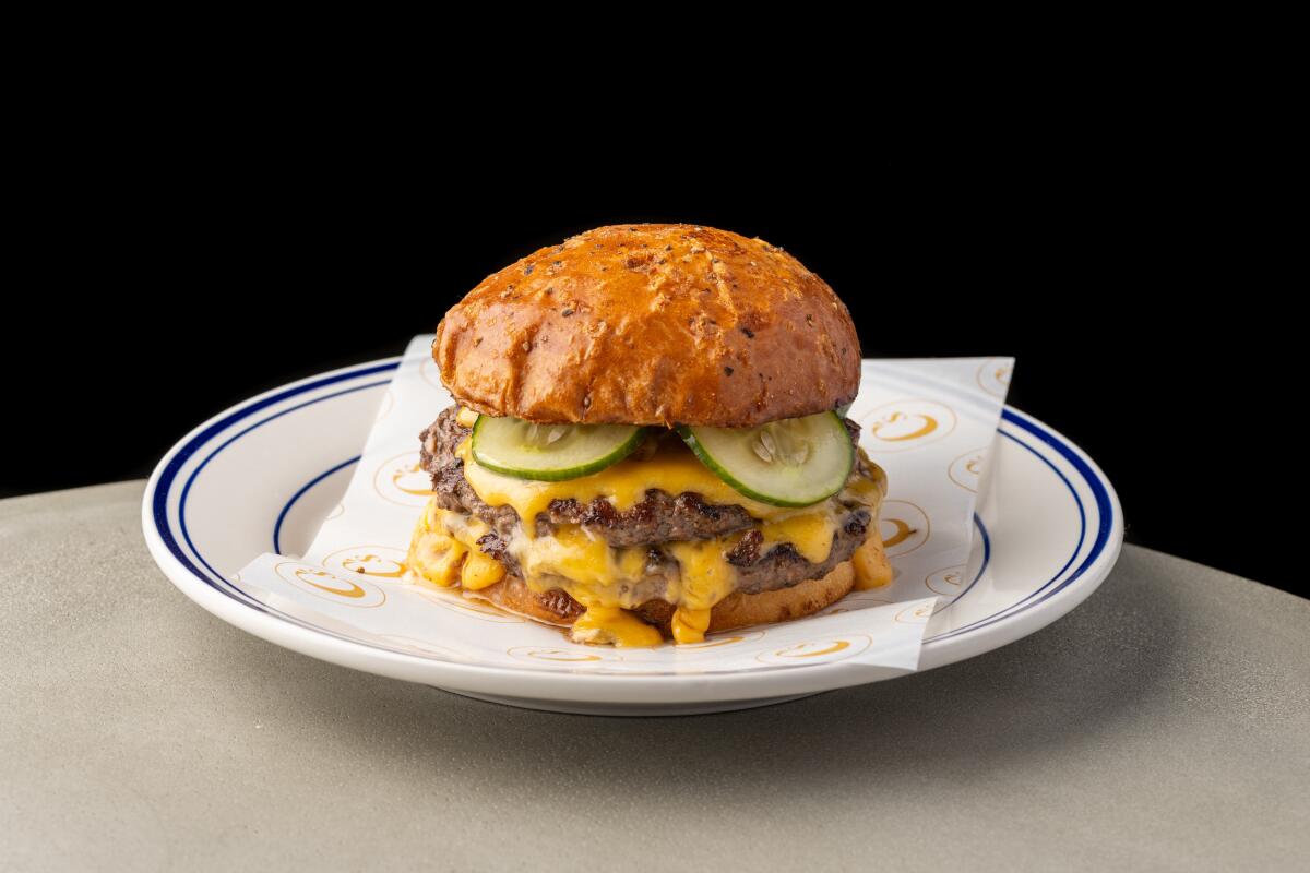 A double cheeseburger with pickle chips on a napkin on a plate