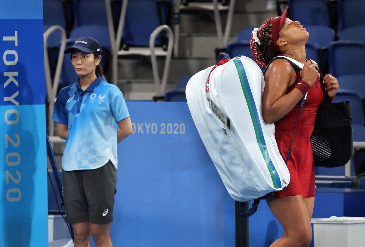 Tennis star Naomi Osaka tilts her head back in frustration while carrying a racket bag