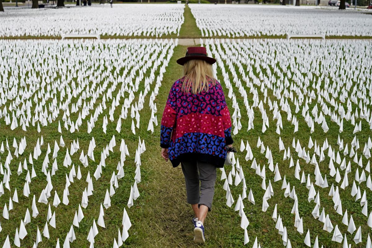 FILE - In this Oct. 27, 2020, Artist Suzanne Brennan Firstenberg walks among thousands of white flags planted in remembrance of Americans who have died of COVID-19 near Robert F. Kennedy Memorial Stadium in Washington. Regardless of the presidential election outcome, a vexing issue remains to be decided: Will the U.S. be able to tame a perilous pandemic that is surging as holidays, winter and other challenges approach? Public health experts fear the answer is no, at least in the short term, with potentially dire consequences. (AP Photo/Patrick Semansky, File)