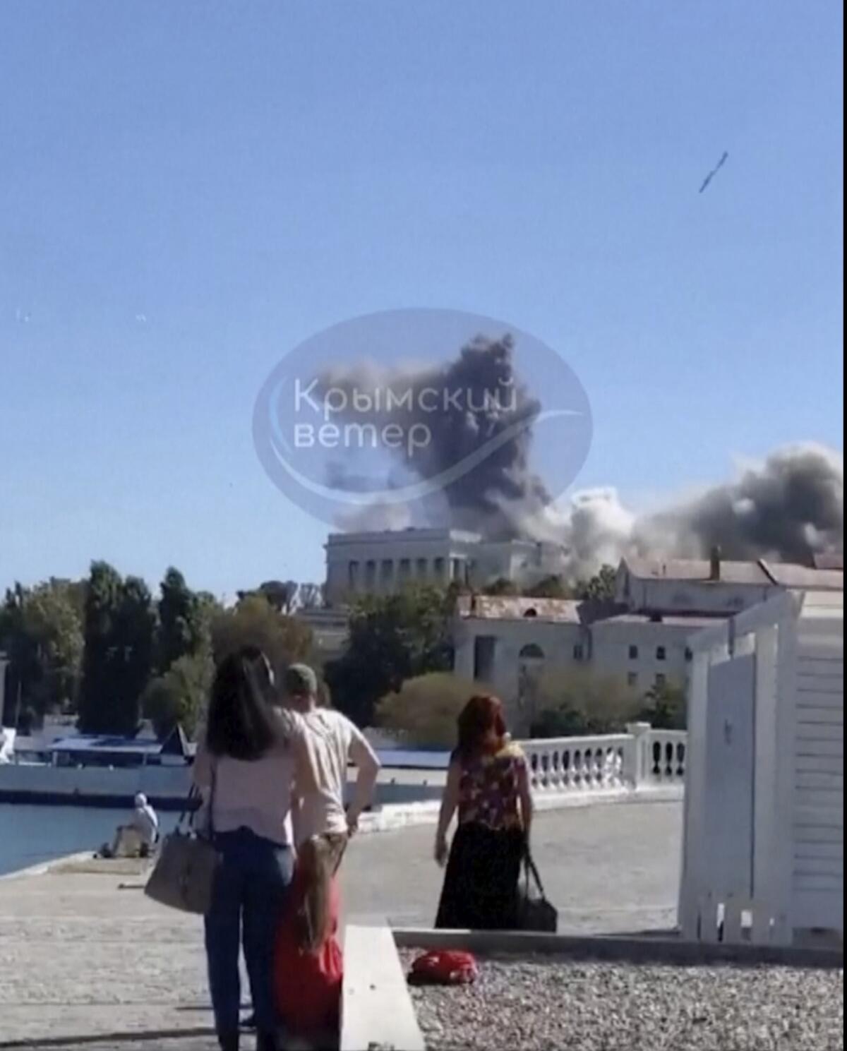 Smoke rises from a building as seaside spectators watch