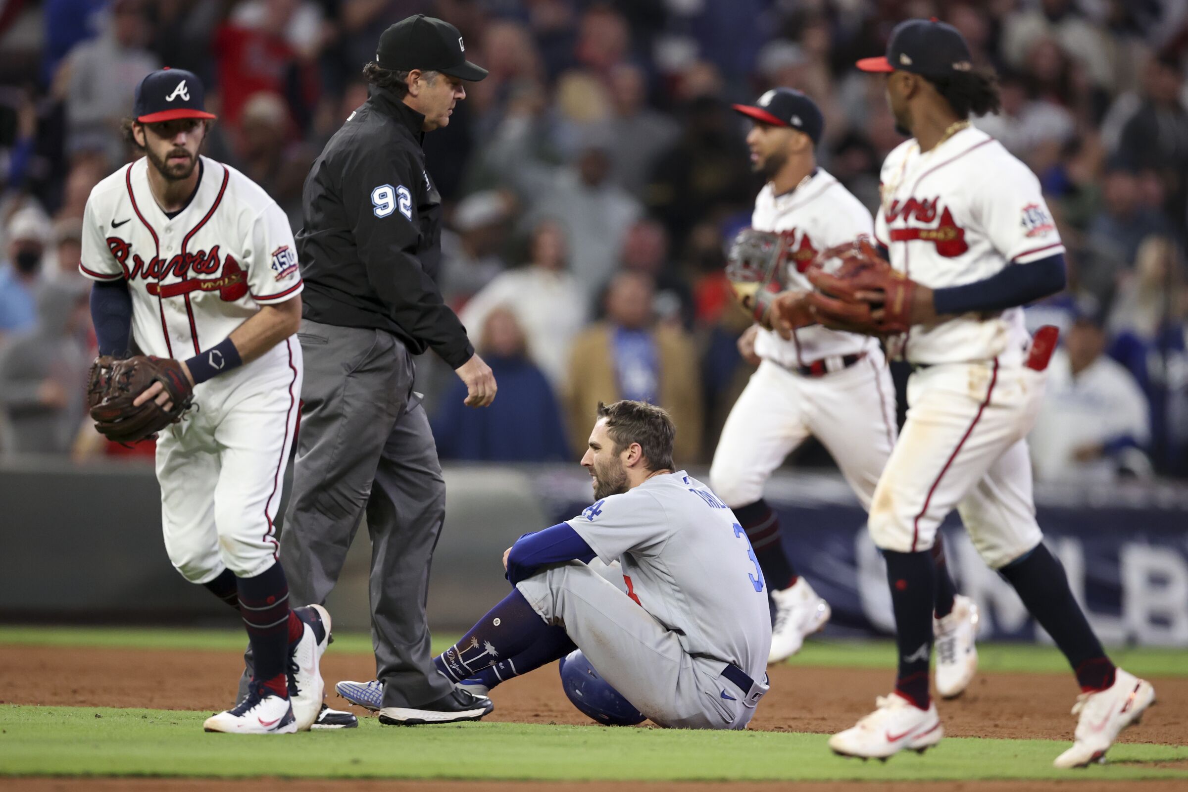 The Dodgers' Chris Taylor sits on the field while Braves players pass him