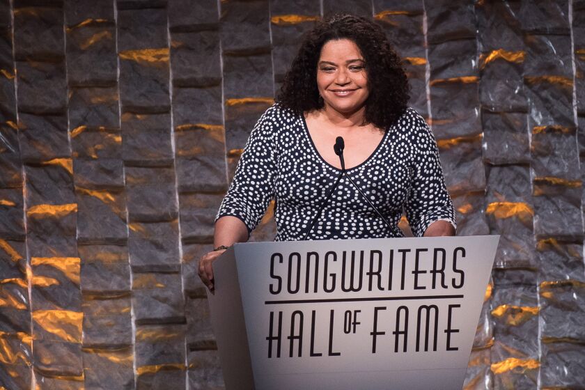 A woman smiles as she stands behind a lectern and microphone at a songwriters hall of fame event
