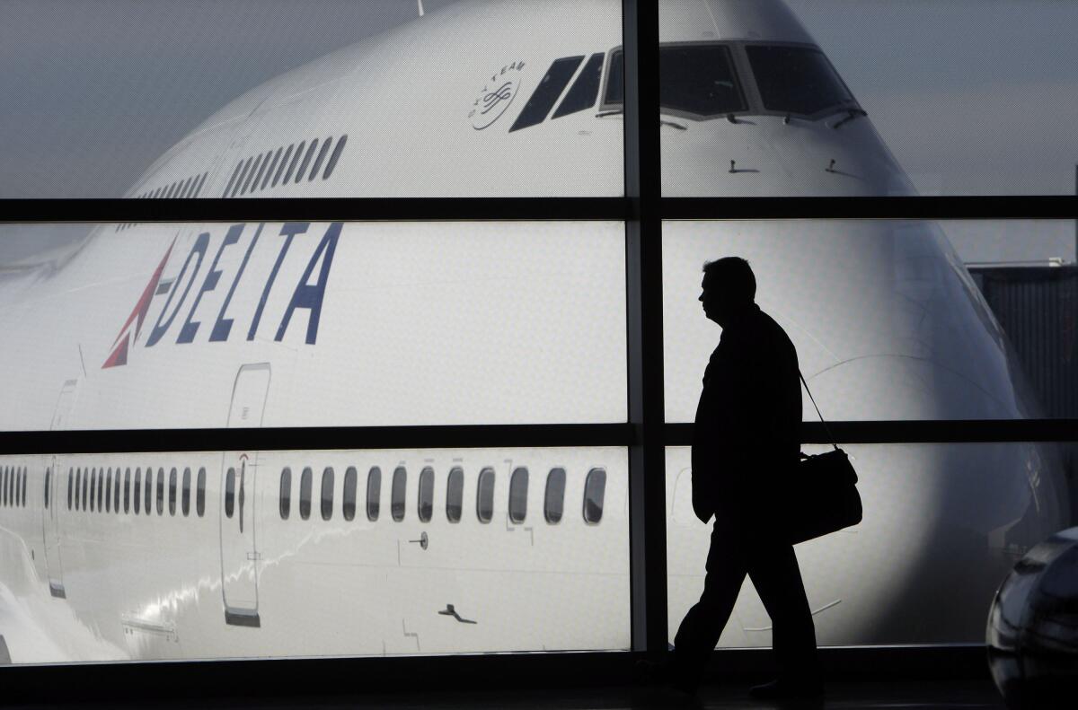 A passenger walks by a window and past a Delta Airlines 747 aircraft.