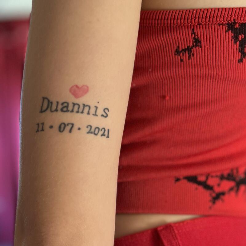 A tattoo shows a heart, the name Duannis, and a date.