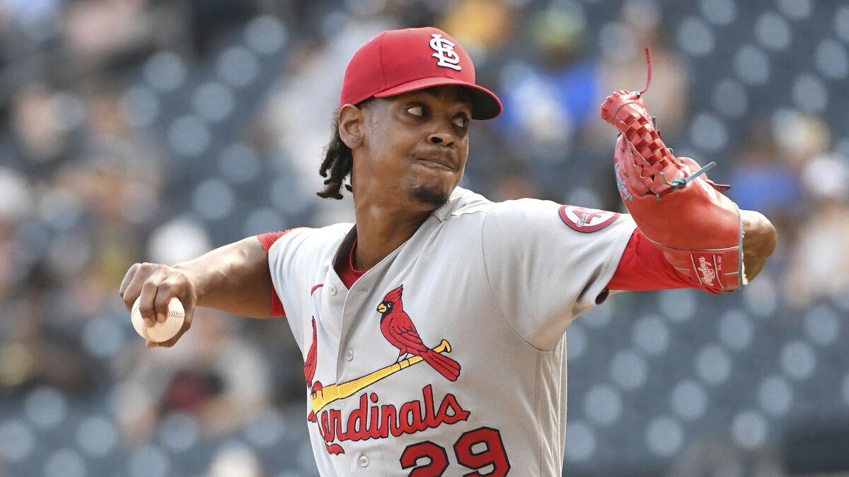 A man throws a baseball while in a red cap as he looks off-camera.