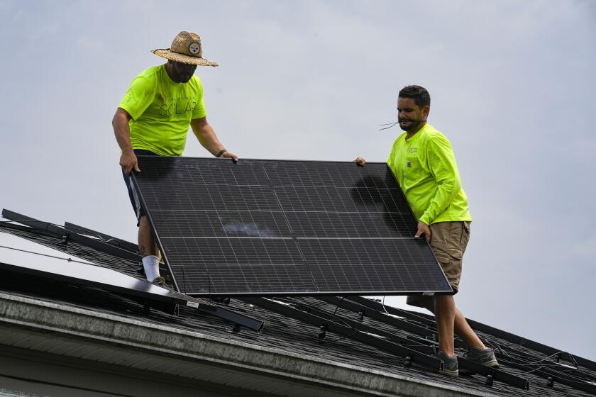 FILE - Even Berrios, left, and Nicholas Hartnett, owner of Pure Power Solar, install a solar panel on the roof of a home in Frankfort, Ky., July 17, 2023. The window to limit human-caused warming to a globally agreed goal is narrowing but still open because of the huge growth of solar energy and electric vehicles sales worldwide, a report said Tuesday, Sept. 26. (AP Photo/Michael Conroy, File)