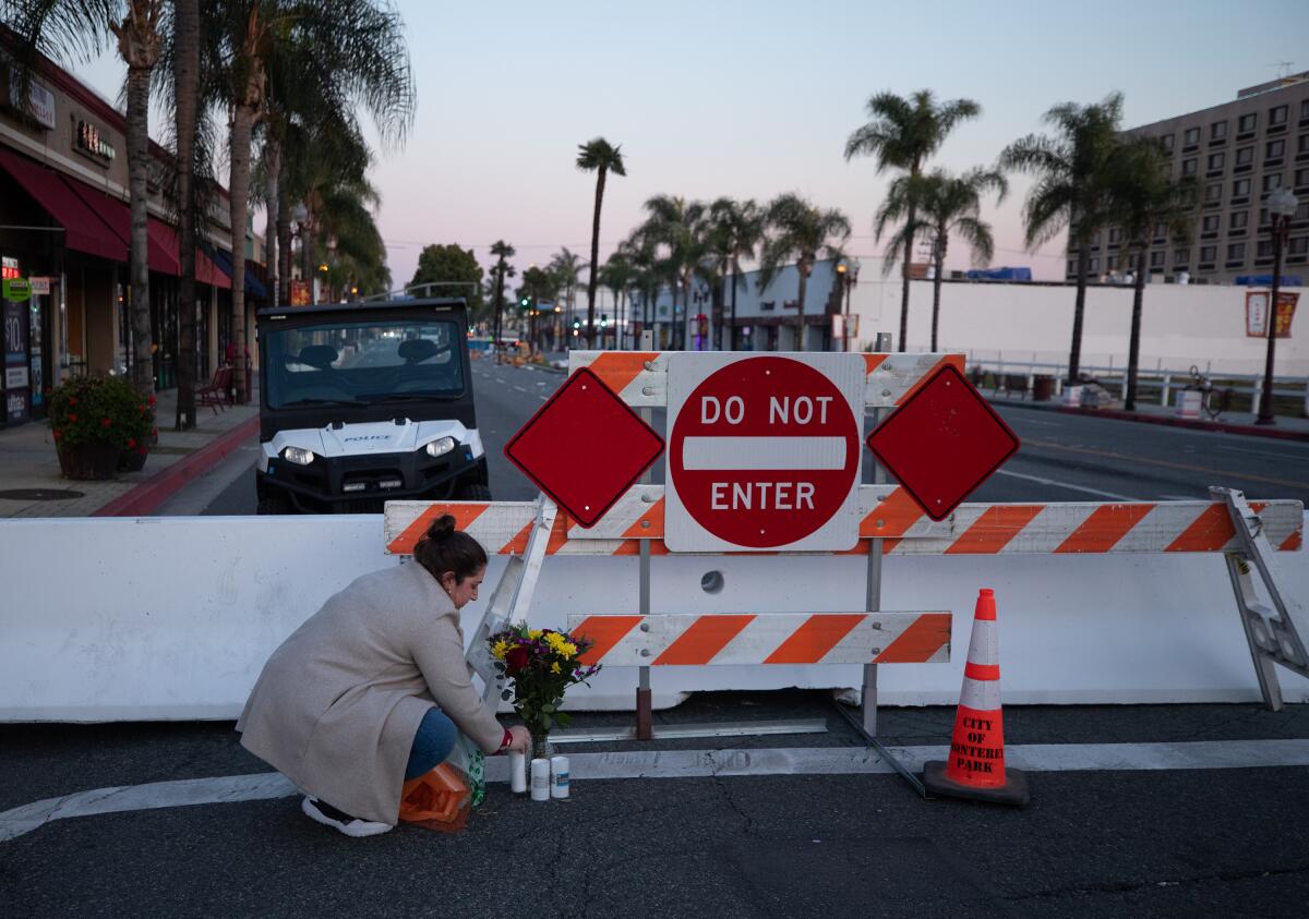 A woman stoops to leave flowers at a street barricade behind a sign reading "Do not enter"