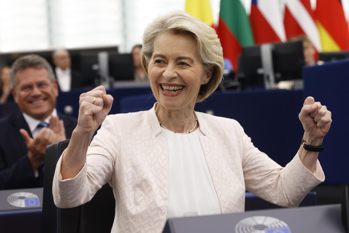 Ursula von der Leyen smiles and raises her clinched fists while standing at a lectern as others applaud