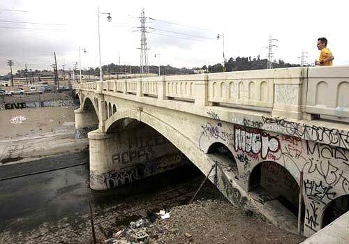 URBAN EYESORE: A jogger crosses the heavily tagged Main Street bridge over the Los Angeles River. The plan envisions widening the channel in places to preserve its flood-control capacity while creating more riparian habitat.