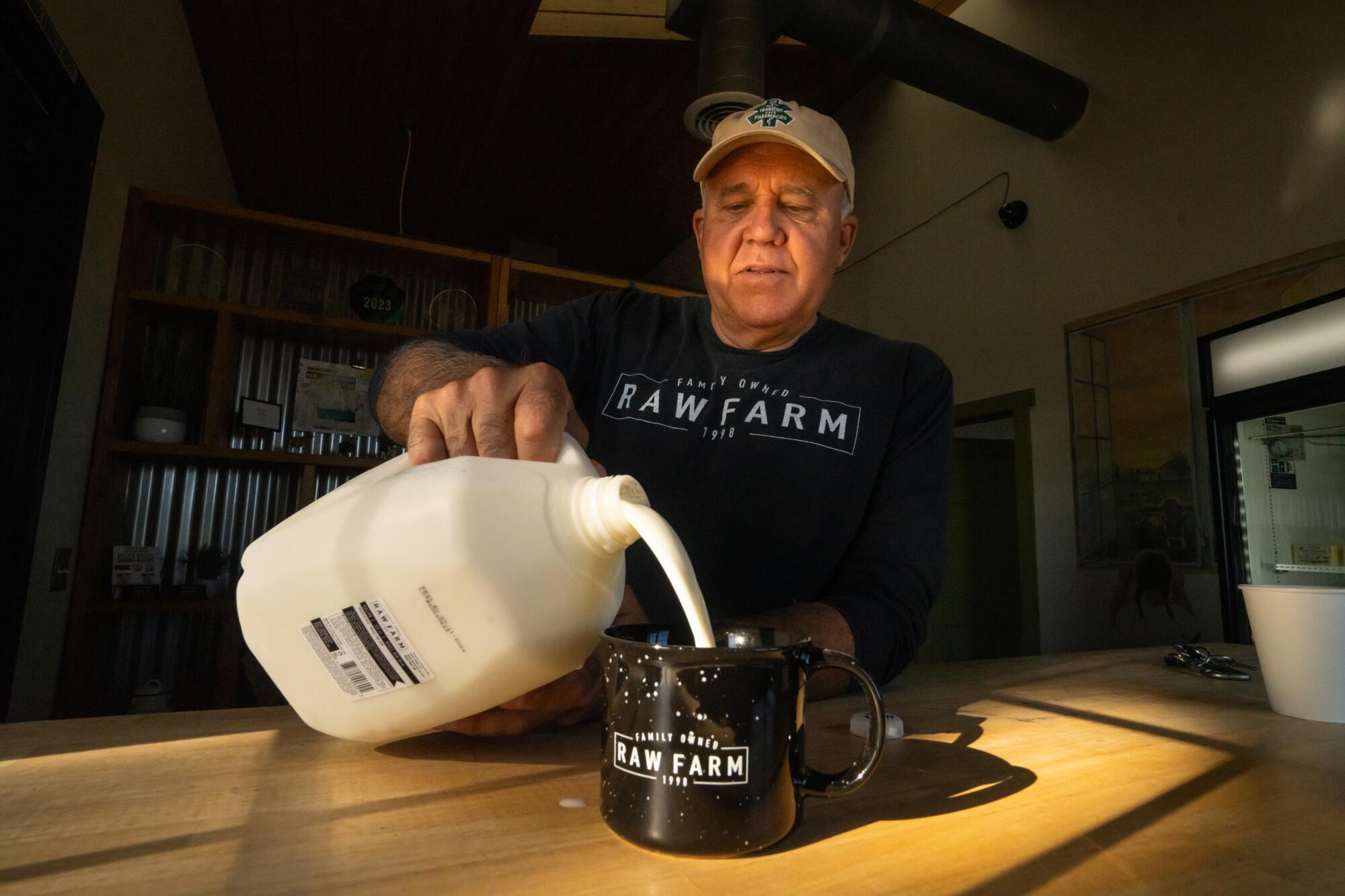 A man sits at a table and pours milk into a mug.