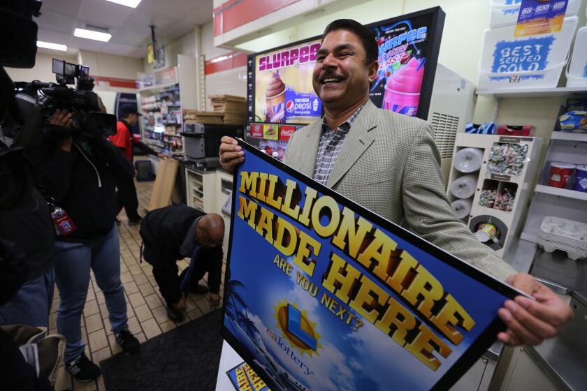 7-Eleven franchise owner Balbir Atwal holds one of the "Millionaire Made Here" lottery signs in his Chino Hills store, where one of the winning Powerball tickets was sold.