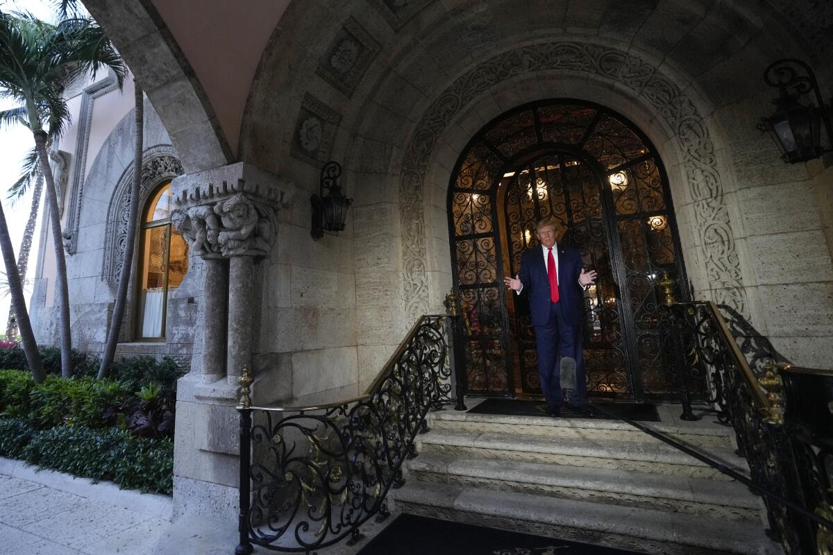 Donald Trump speaks in an ornate doorway while holding his hands out.