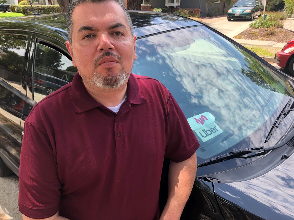 Robert Moreno stands in front of a car with Uber and Lyft stickers.