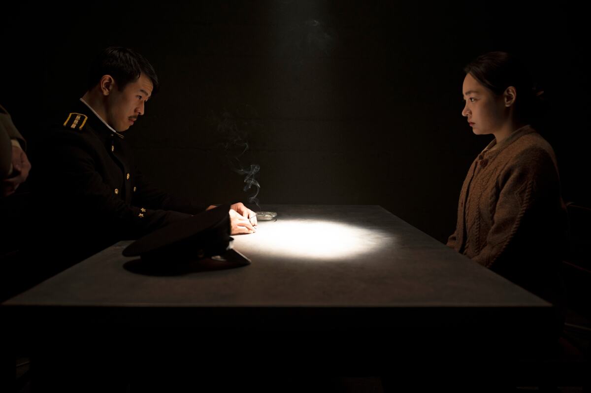 A man and a woman, in shadow, sit at a table whose top is illuminated.