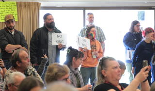 People at a town hall meeting hold signs with the words "No King."