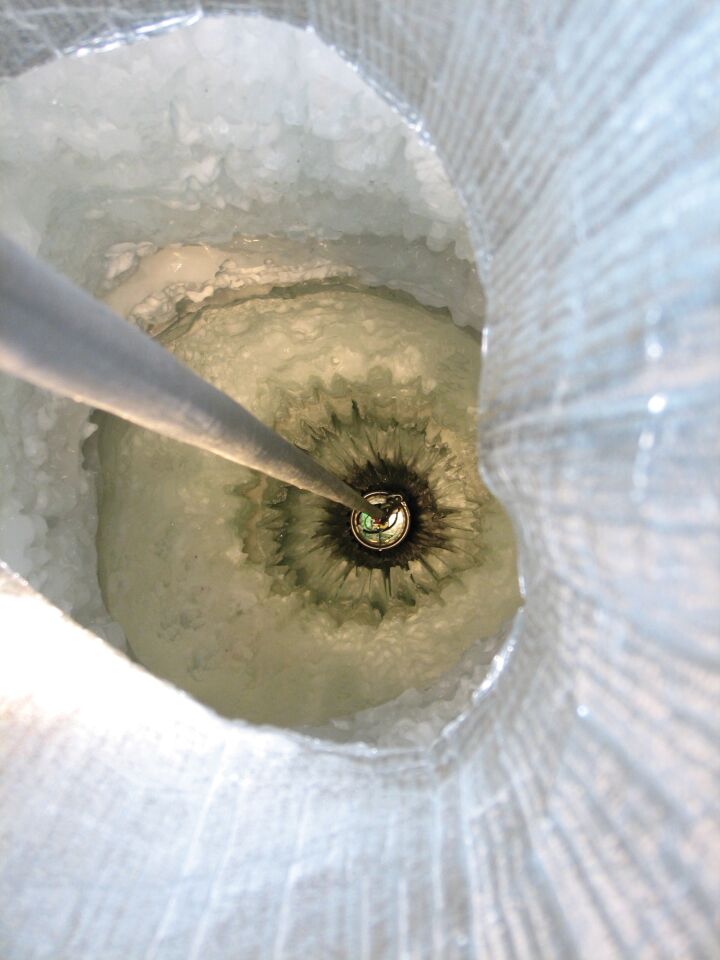 A digital optical module, or DOM, is lowered into the hole of an IceCube string. The IceCube detector consists of 86 strings of DOMs, which look for light when neutrinos strike the ice.