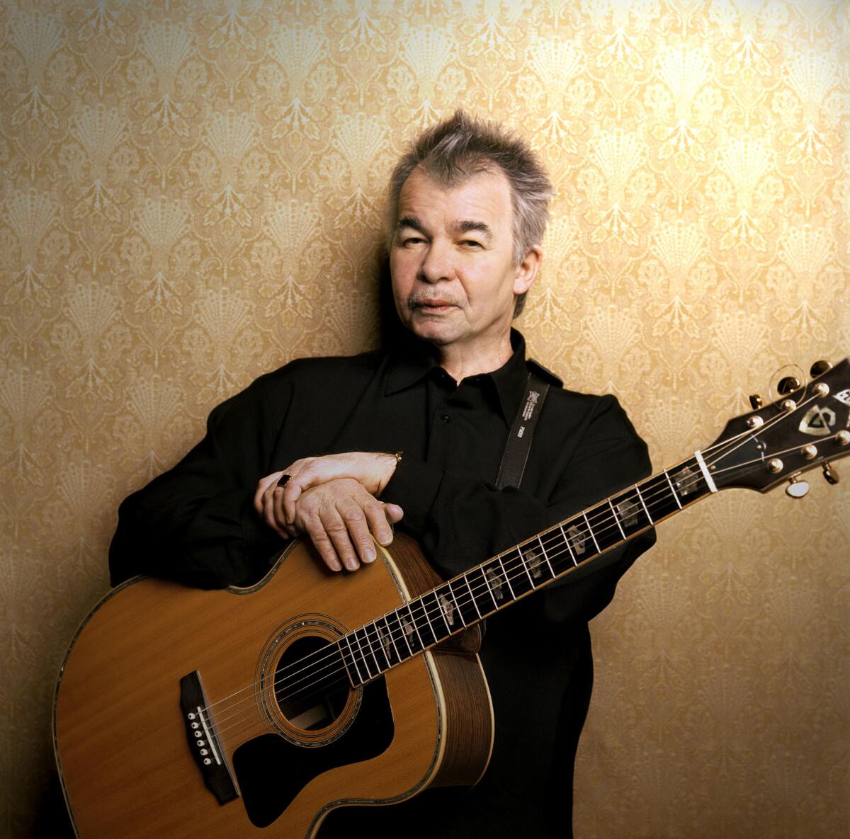 John Prine poses with a guitar strapped around his neck.