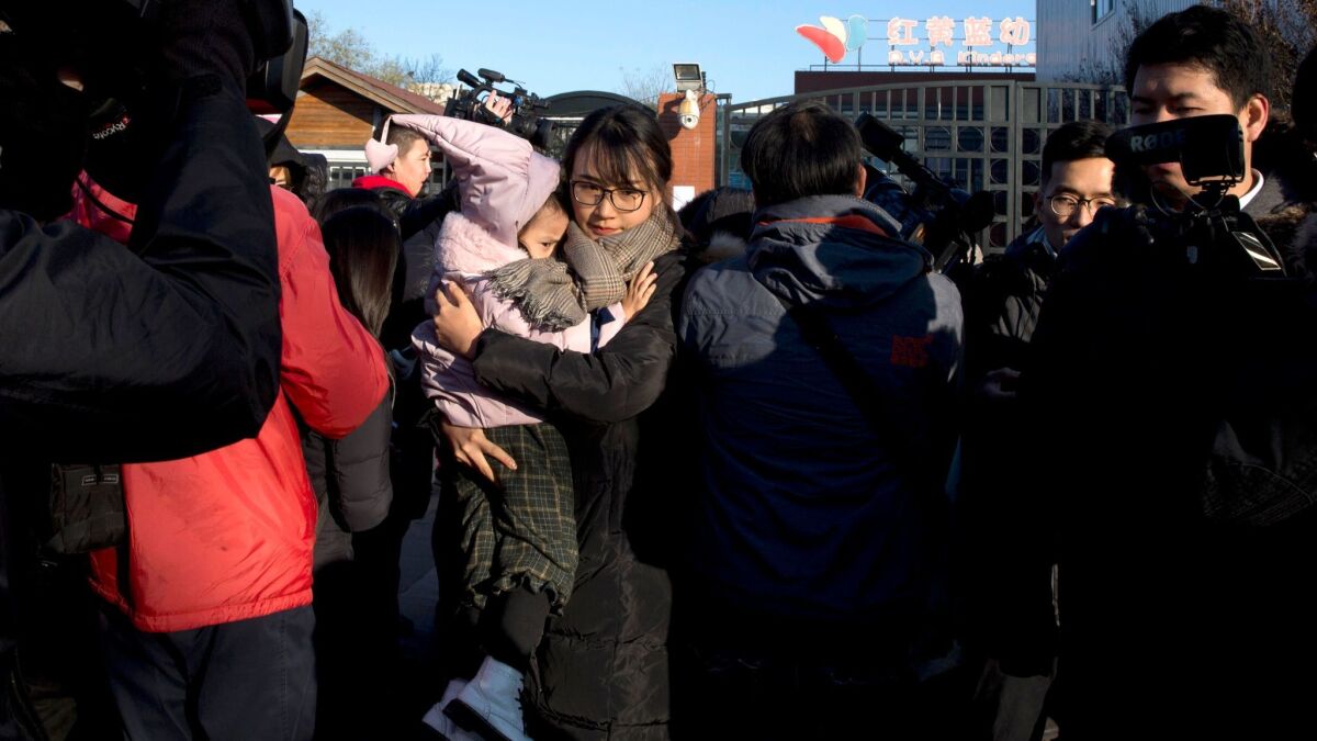 A woman leaves with a child after telling the media she came to withdraw the child from the RYB kindergarten in Beijing on Friday, Nov. 24, 2017. The school has suspended three teachers.