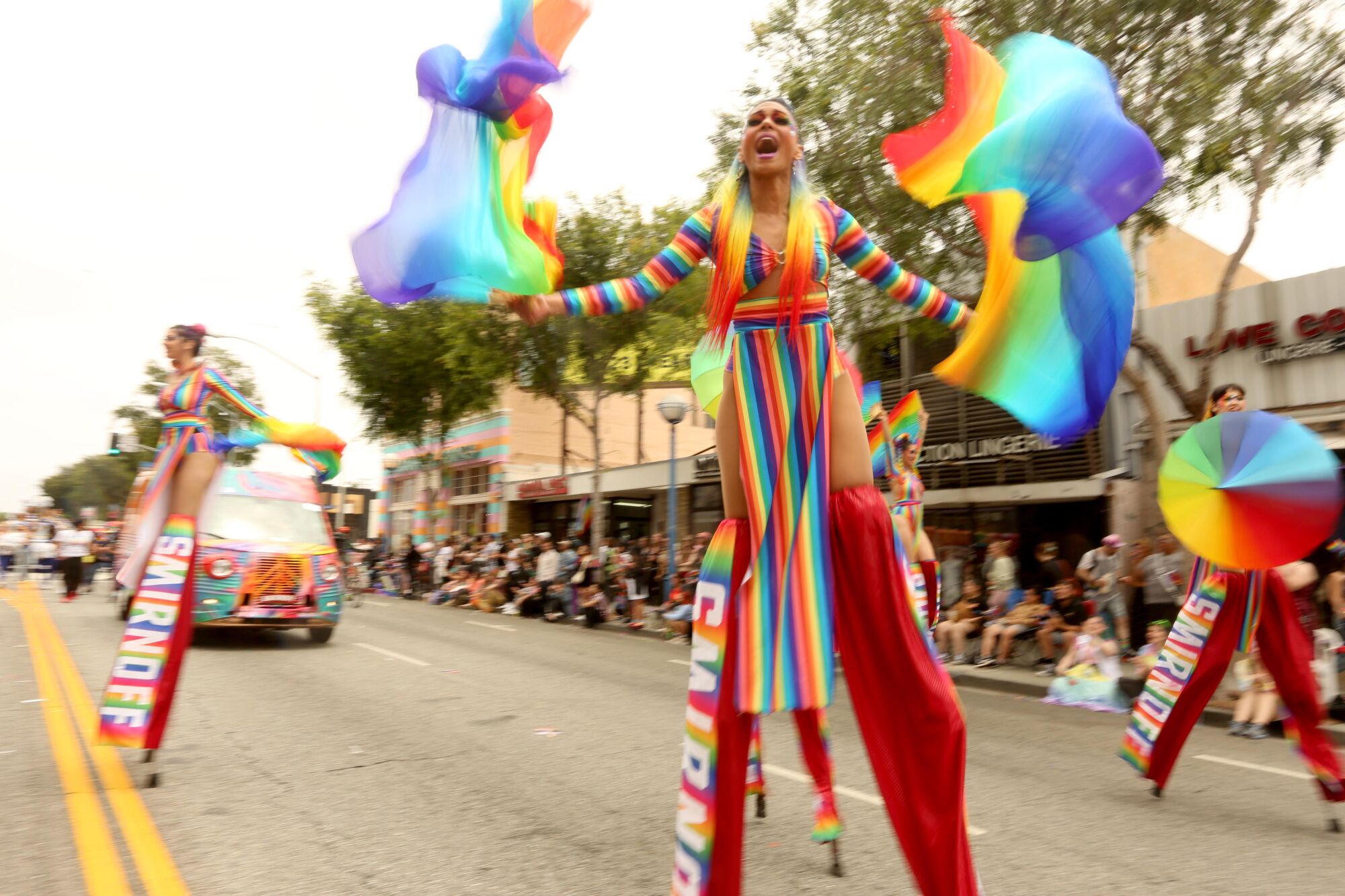 A person in rainbow clothing waves flags.