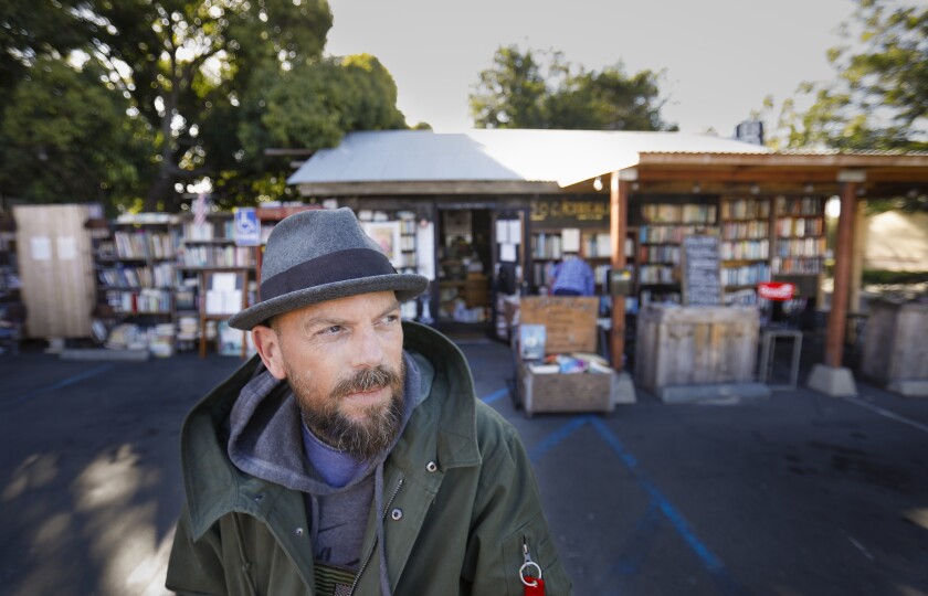 Sean Christopher, the owner of Lhooq Books, a funky vintage bookstore and arts hub in Carlsbad Village, sits in front of his shop in October. Christopher lost his lease on the property on Nov. 16, but his landlord has granted him a seven-month reprieve to find the business a new home.