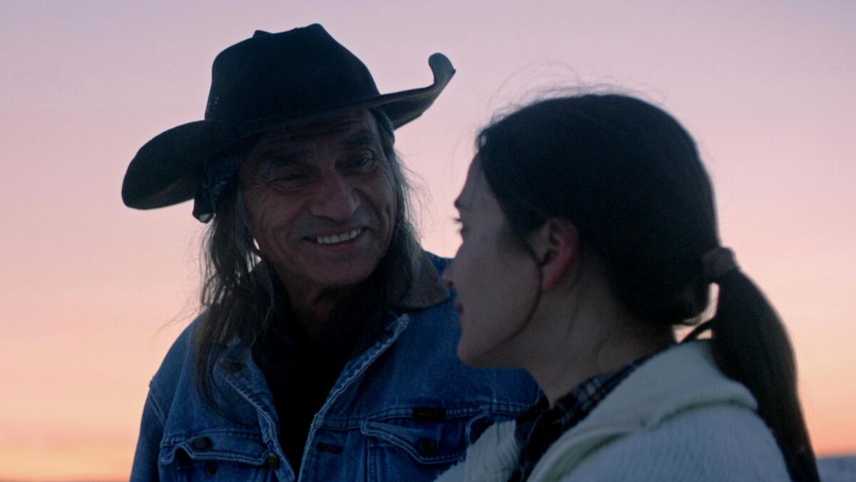 A man in a cowboy hat smiles at a women at dusk.
