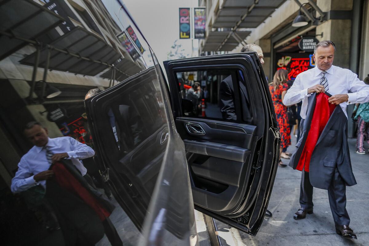 A man holds a suit jacket next to a vehicle with an open door.