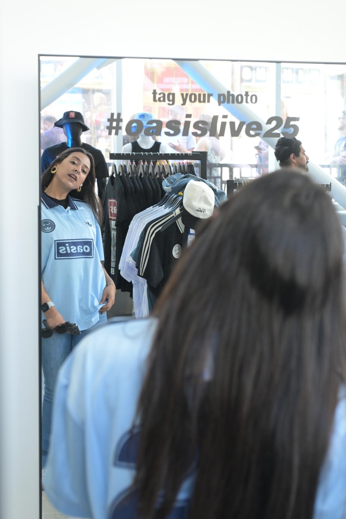 An Oasis fan models her new shirt in the mirror at the Hollywood pop-up shop.