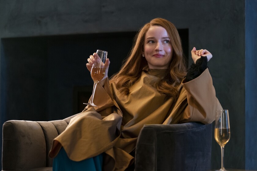 A seated red-haired woman smiles and holds a champagne flute.