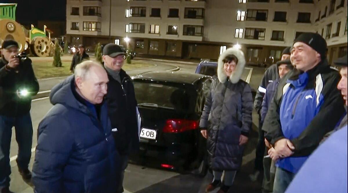 People in coats on a sidewalk talk to Vladimir Putin.
